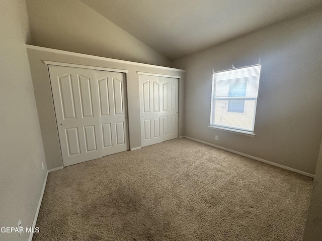 unfurnished bedroom with multiple closets, vaulted ceiling, carpet flooring, and baseboards