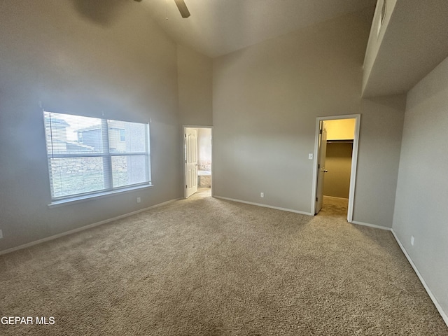 unfurnished bedroom featuring high vaulted ceiling, carpet floors, baseboards, a walk in closet, and ceiling fan