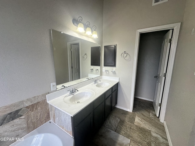 full bath featuring double vanity, baseboards, stone finish flooring, and a tub