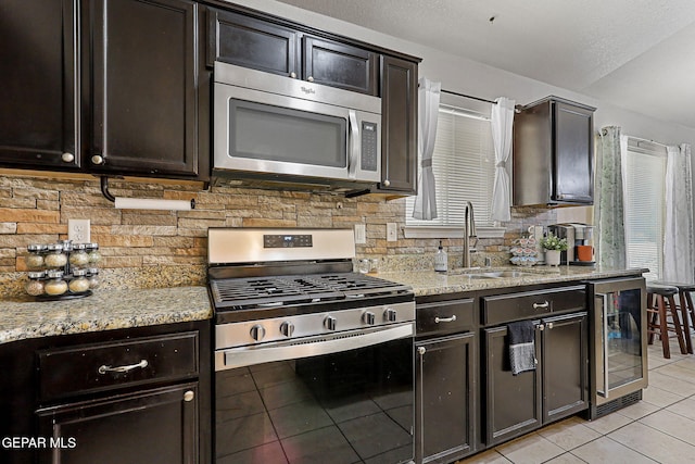kitchen with light tile patterned flooring, a sink, beverage cooler, stainless steel appliances, and backsplash