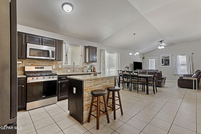 kitchen featuring backsplash, vaulted ceiling, light tile patterned floors, open floor plan, and stainless steel appliances