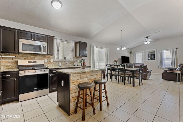 kitchen featuring lofted ceiling, open floor plan, light tile patterned floors, appliances with stainless steel finishes, and backsplash