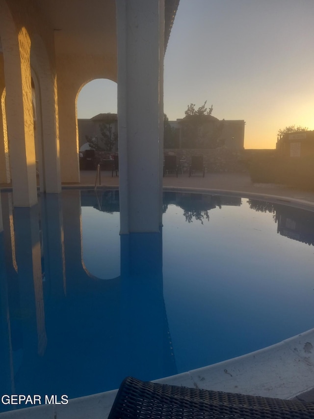 pool at dusk featuring an outdoor pool and a patio
