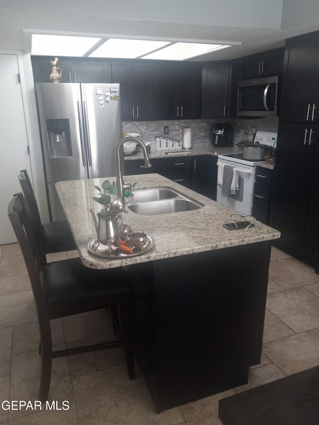 kitchen with appliances with stainless steel finishes, a sink, dark cabinetry, a breakfast bar, and backsplash