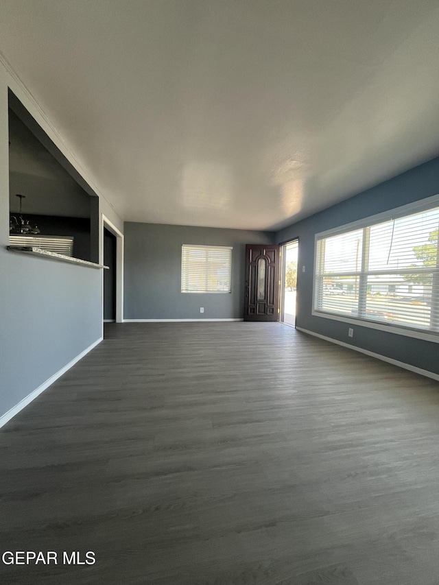 unfurnished living room with baseboards and dark wood-type flooring