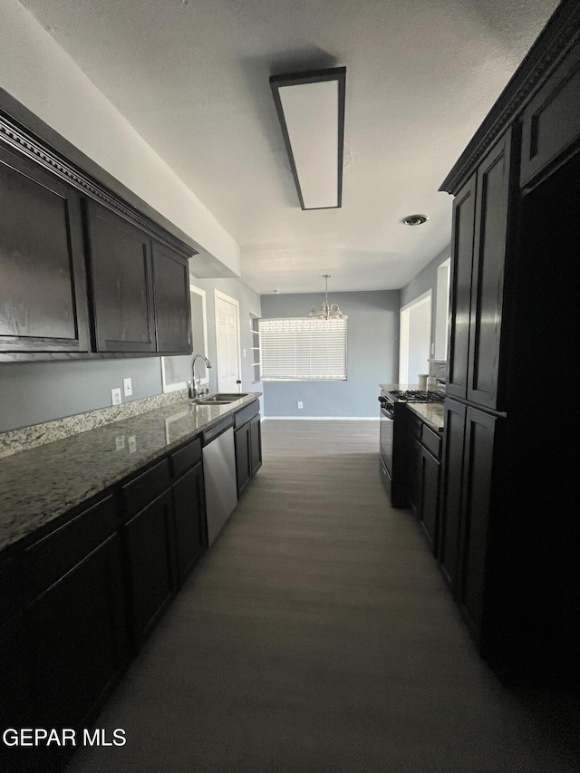 kitchen with appliances with stainless steel finishes, a sink, dark cabinetry, stone counters, and wood finished floors