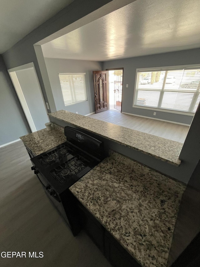 kitchen featuring gas stove, baseboards, stone countertops, and wood finished floors