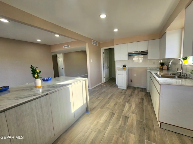 kitchen featuring white cabinets, a sink, light wood-type flooring, backsplash, and visible vents