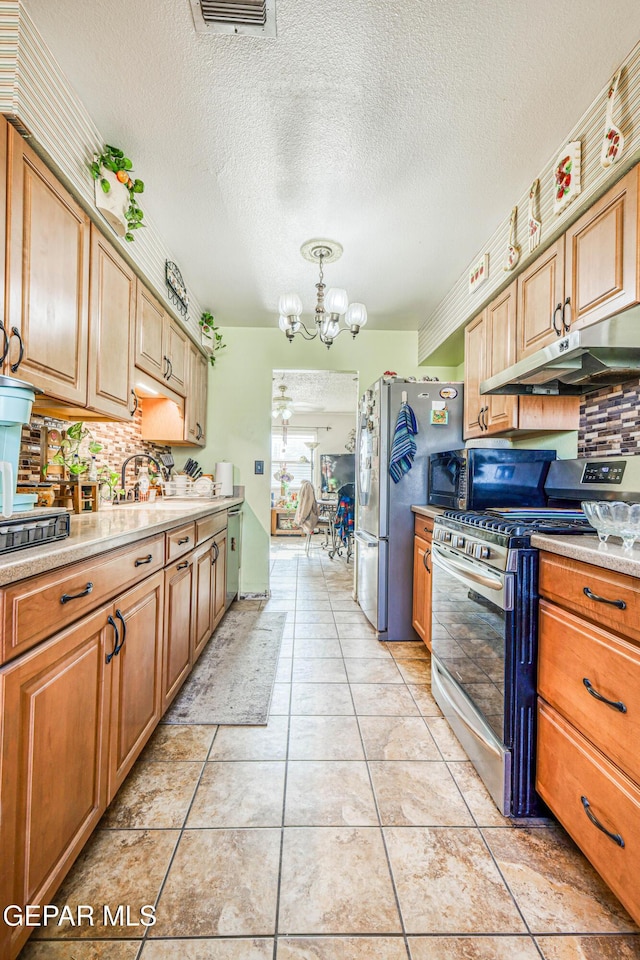 kitchen with backsplash, stainless steel gas range oven, light countertops, a chandelier, and under cabinet range hood
