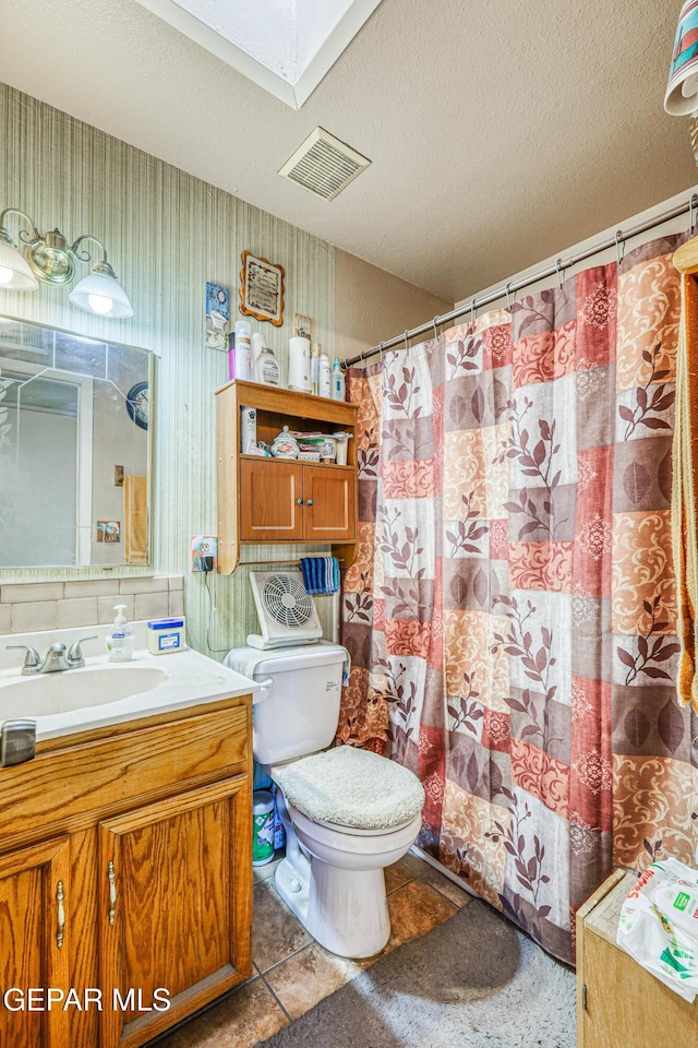 full bathroom featuring visible vents, vanity, toilet, a textured ceiling, and a skylight