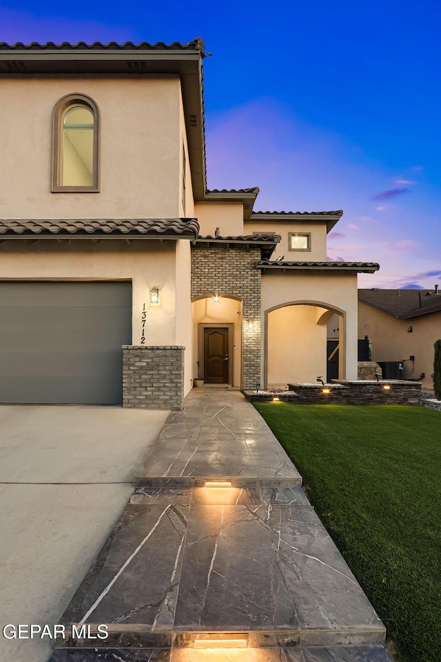 view of front of home with a garage, stucco siding, concrete driveway, a tiled roof, and a yard
