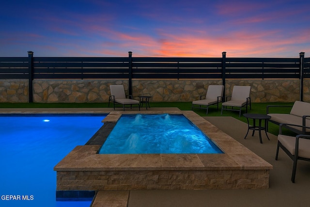 pool at dusk with a hot tub