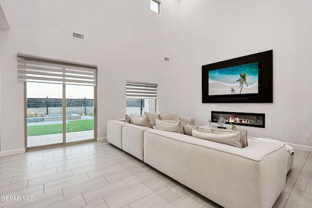 living area with visible vents, baseboards, a glass covered fireplace, and a towering ceiling
