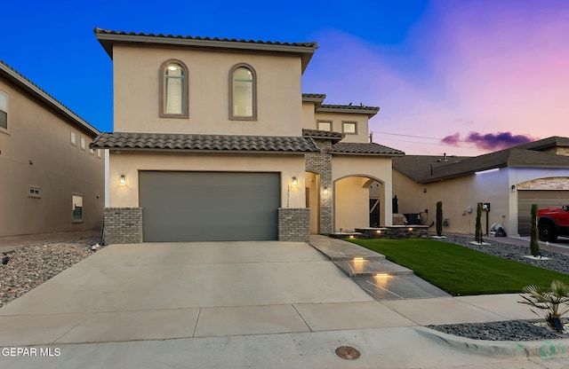mediterranean / spanish house with a tiled roof, a lawn, a garage, concrete driveway, and stucco siding