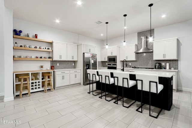 kitchen with wall chimney range hood, a sink, stainless steel appliances, backsplash, and visible vents