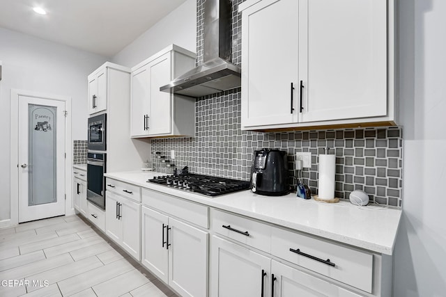 kitchen with wall chimney range hood, white cabinets, appliances with stainless steel finishes, and decorative backsplash