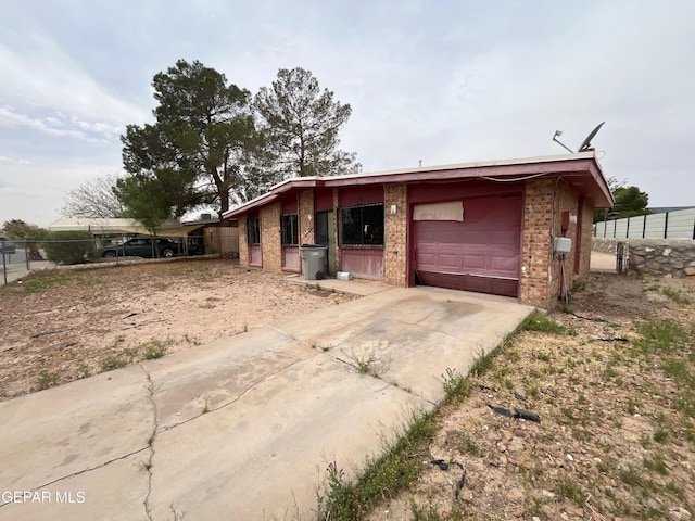 mid-century inspired home with concrete driveway, brick siding, an attached garage, and fence