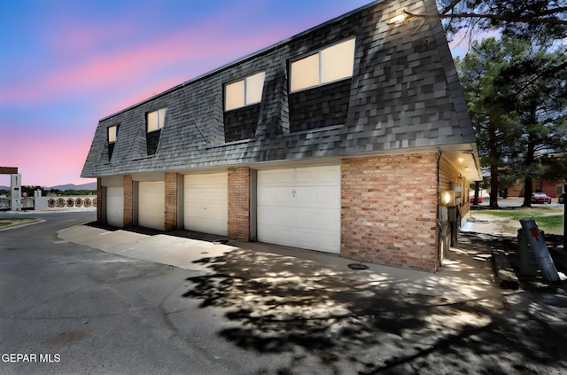 view of front of home with roof with shingles, brick siding, mansard roof, aphalt driveway, and an attached garage