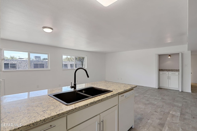 kitchen with light stone countertops, white dishwasher, white cabinetry, a sink, and light wood-style flooring