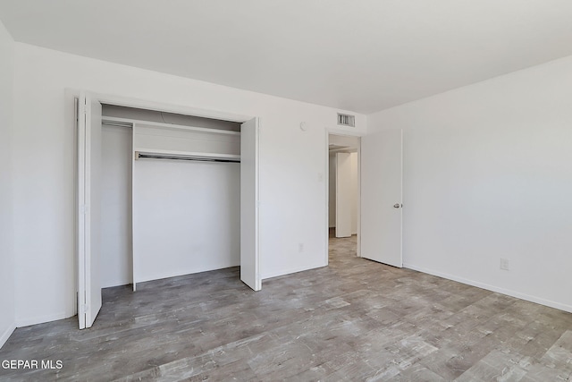 unfurnished bedroom with visible vents, wood finished floors, and a closet