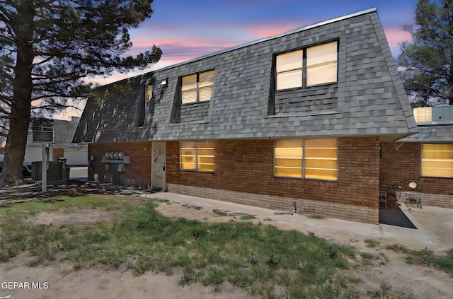 back of house with brick siding, mansard roof, and roof with shingles
