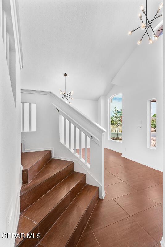 staircase with tile patterned floors, a notable chandelier, baseboards, and vaulted ceiling