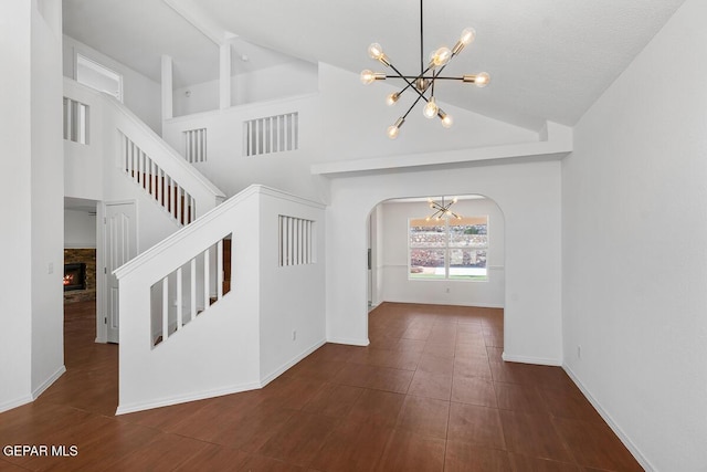 entryway featuring lofted ceiling, a fireplace, baseboards, arched walkways, and a notable chandelier
