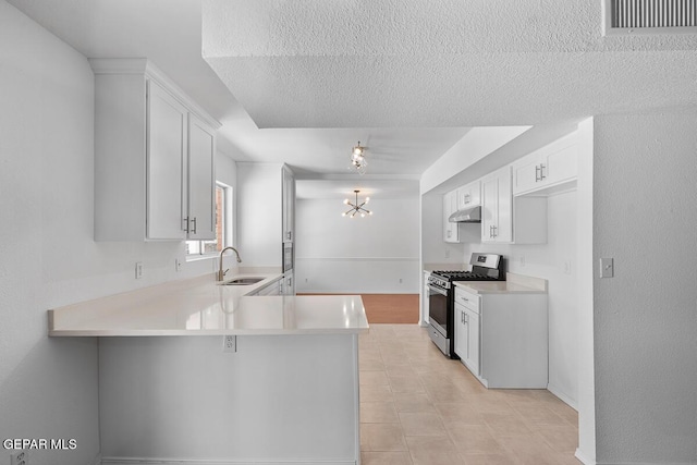 kitchen featuring a sink, stainless steel gas range oven, light countertops, a peninsula, and under cabinet range hood