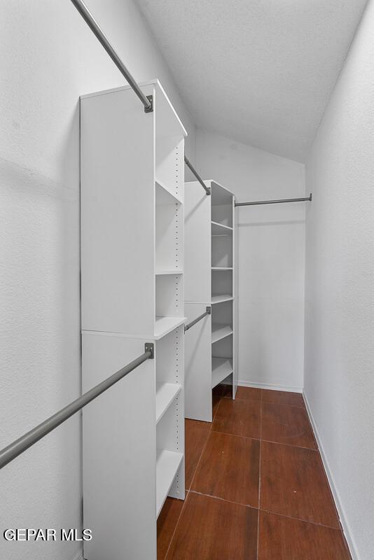 spacious closet with dark wood finished floors and vaulted ceiling