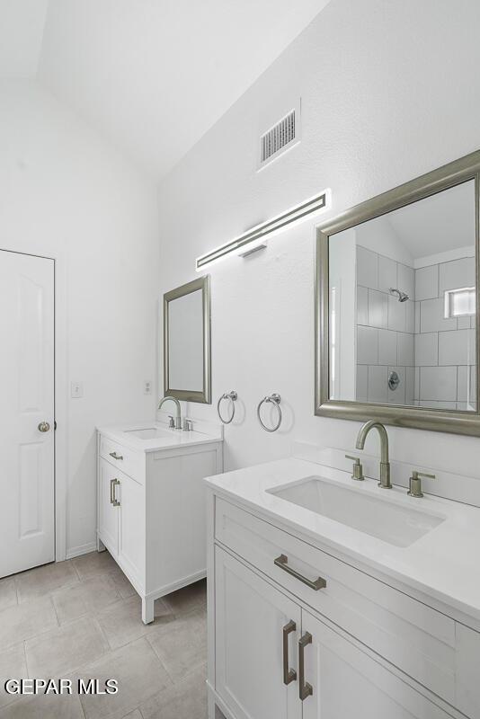 bathroom featuring vaulted ceiling, two vanities, and a sink
