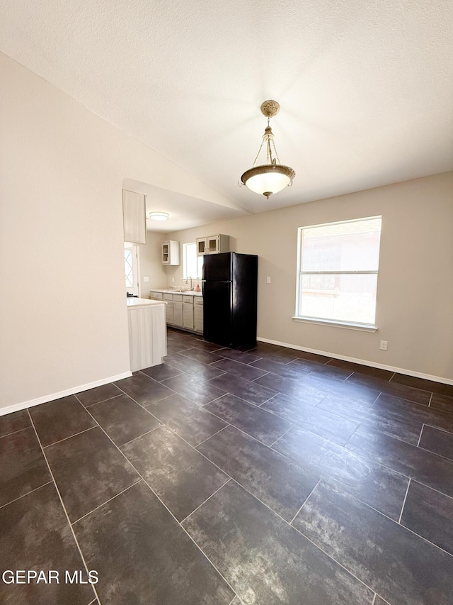 unfurnished living room featuring dark tile patterned floors, baseboards, vaulted ceiling, and a sink