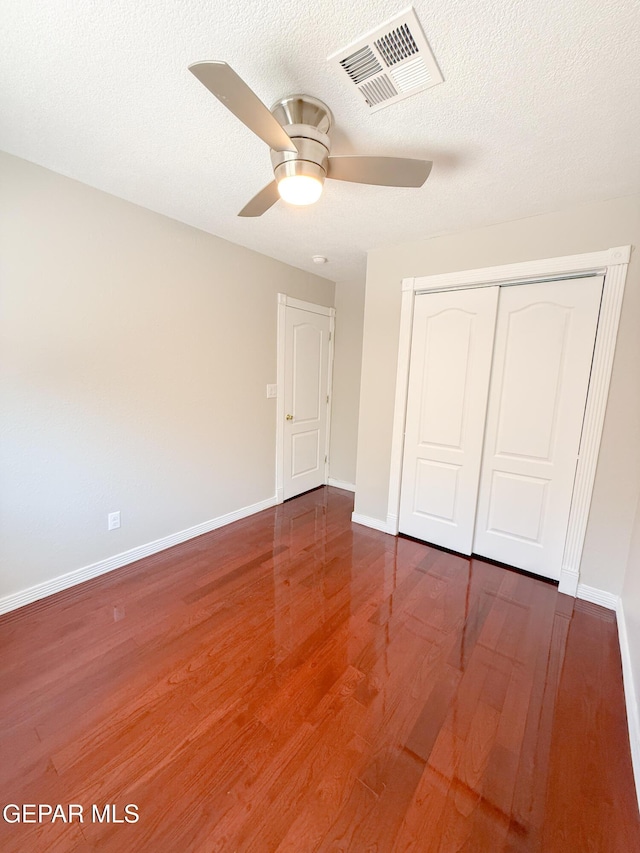 unfurnished bedroom featuring a ceiling fan, baseboards, wood finished floors, visible vents, and a closet