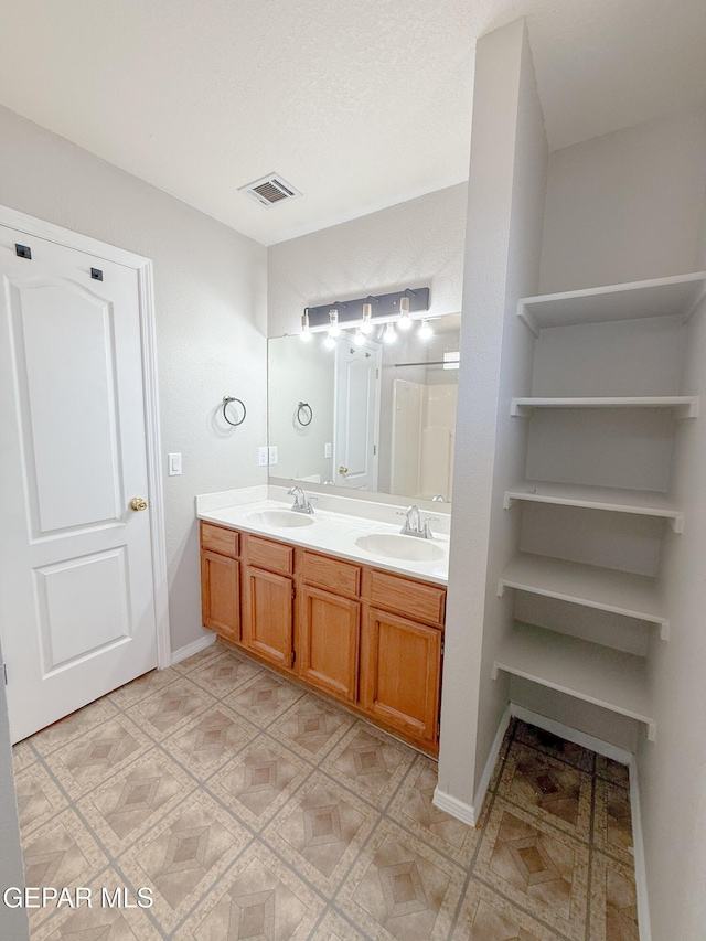 full bath with a sink, baseboards, double vanity, and visible vents