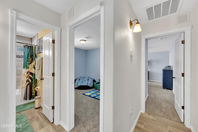 hall with baseboards, visible vents, and wood finished floors