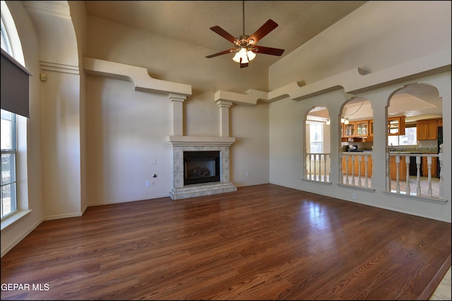 unfurnished living room with a ceiling fan, baseboards, a tiled fireplace, a towering ceiling, and wood finished floors