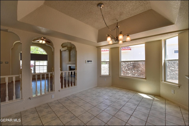 unfurnished dining area featuring a textured ceiling, ceiling fan with notable chandelier, tile patterned floors, arched walkways, and a fireplace
