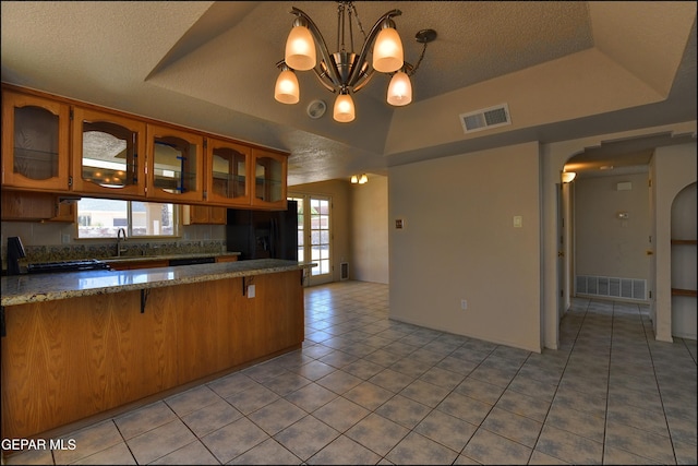 kitchen with a textured ceiling, black refrigerator with ice dispenser, arched walkways, and visible vents