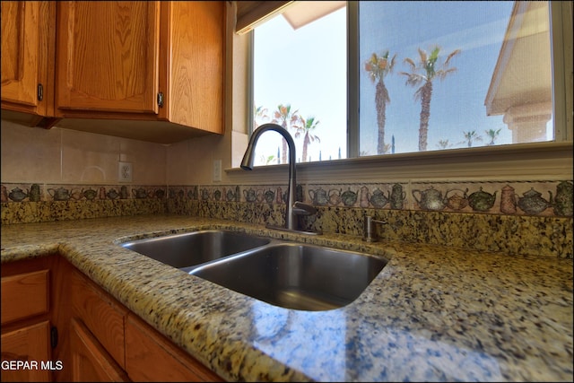 kitchen featuring backsplash, brown cabinetry, light stone countertops, and a sink