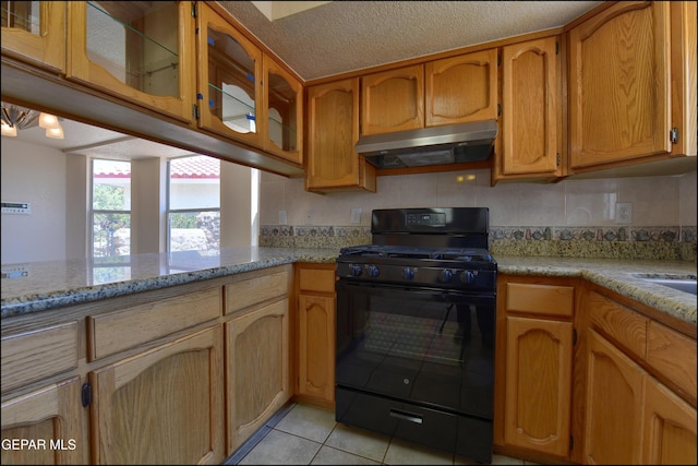 kitchen featuring black gas range oven, glass insert cabinets, light tile patterned floors, under cabinet range hood, and light stone counters