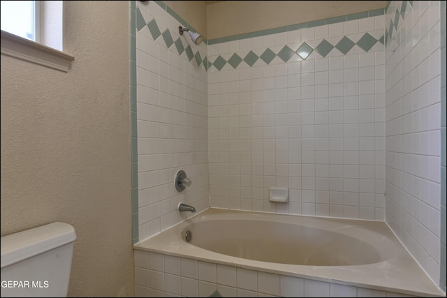 bathroom with toilet, shower / washtub combination, and a textured wall