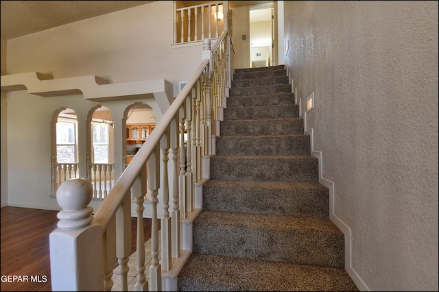 stairway with a towering ceiling, a textured wall, and wood finished floors