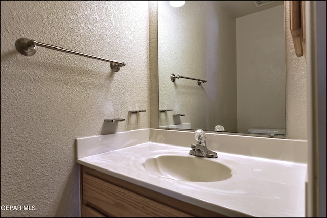bathroom with toilet, vanity, and a textured wall
