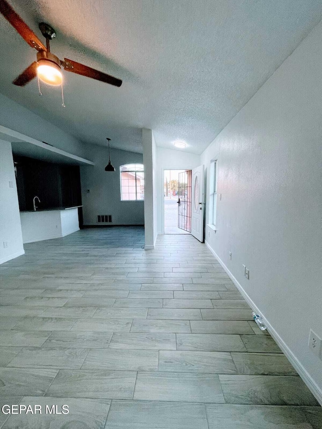 unfurnished living room with visible vents, a ceiling fan, baseboards, and a textured ceiling
