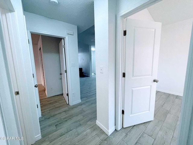 hallway with baseboards, light wood-type flooring, and a textured ceiling