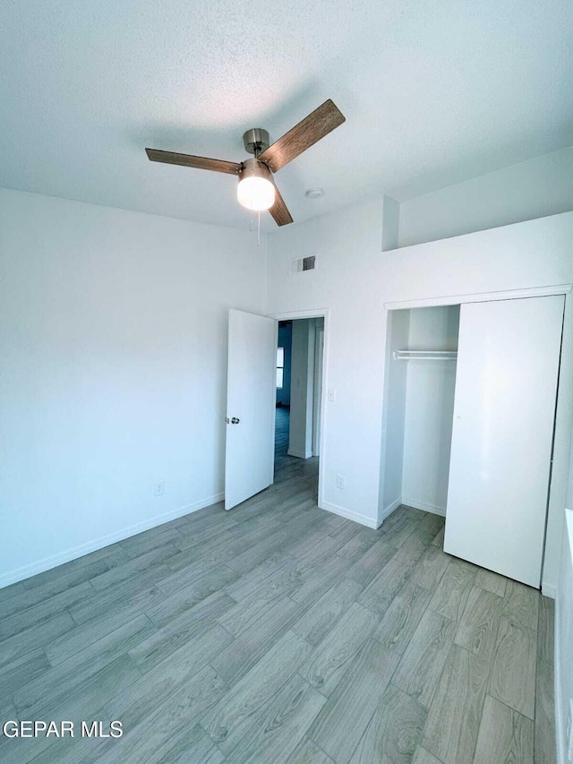unfurnished bedroom with ceiling fan, a textured ceiling, wood finished floors, visible vents, and a closet