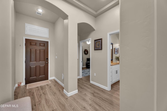entryway featuring arched walkways, baseboards, visible vents, and light wood-type flooring