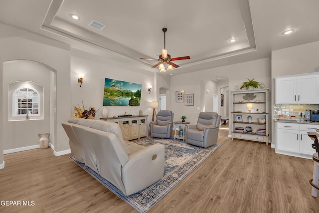 living area with a raised ceiling, arched walkways, recessed lighting, light wood-type flooring, and visible vents