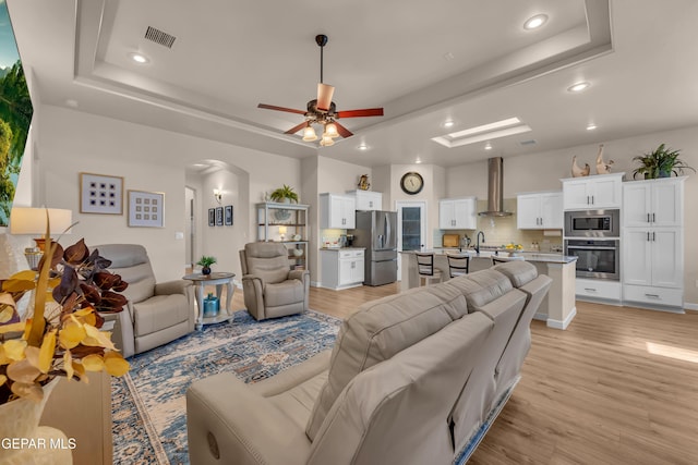 living room featuring a raised ceiling, light wood-style floors, arched walkways, recessed lighting, and a ceiling fan