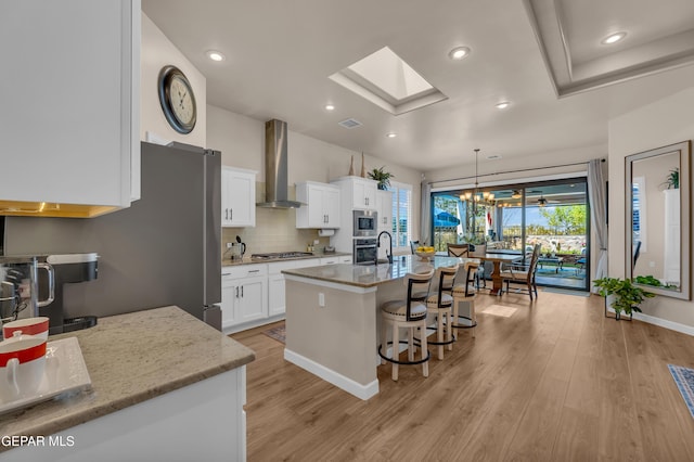 kitchen with light wood-style floors, a breakfast bar area, wall chimney range hood, and stainless steel appliances
