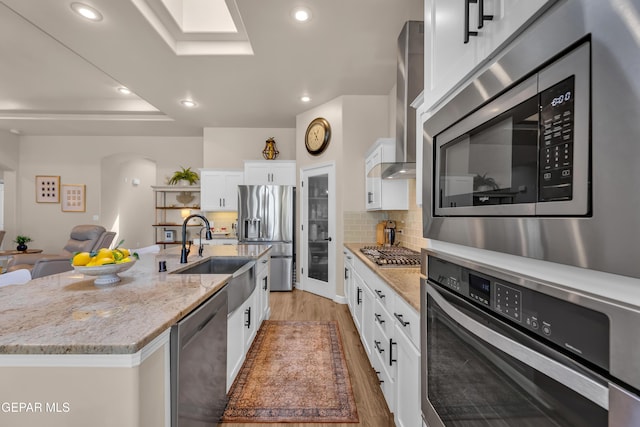 kitchen with wall chimney range hood, arched walkways, a sink, light wood-style floors, and stainless steel appliances